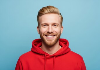 Naklejka na ściany i meble Portrait of a smiling young man with blonde hair and beard wearing a red hooded sweatshirt against a blue background of mockup