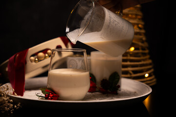 Pouring rompope into glass, mexican christmas beverage with festive decorations
