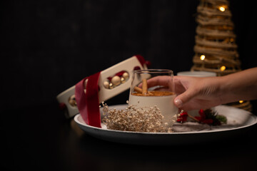 Hand grabbing glass of rompope with christmas decorations on a tray