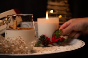 Glass of rompope with cinnamon sticks, christmas decoration and candle burning