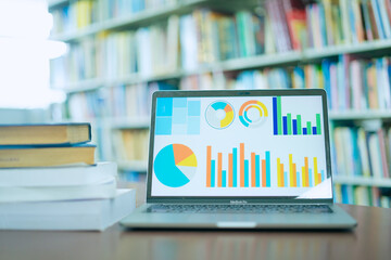 A laptop screen displaying a graph and a book placed on the table in the library, representing a business concept.	