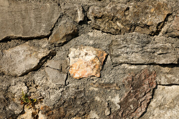 Rough stone wall built with irregular rocks and gray concrete mortar, ideal for backgrounds that emphasize natural texture and rugged design.
