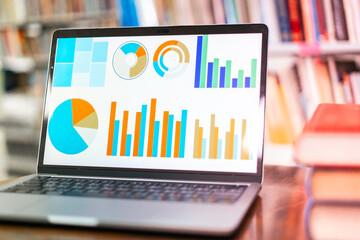 A laptop screen displaying a graph and a book placed on the table in the library, representing a business concept.	
