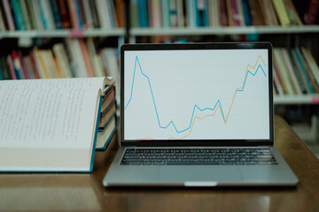 A laptop screen displaying a graph and a book placed on the table in the library, representing a business concept.	