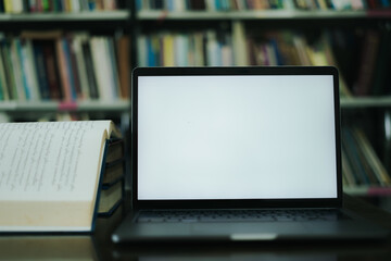 There is a laptop with a white screen and a book placed on the table in the library.