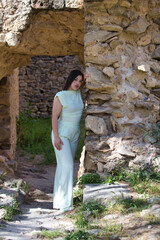 A beautiful Spanish teenager with long dark hair rests her hand on a stone wall and looks sad and serious. The young woman is alone, suffering from mental health issues and depression.