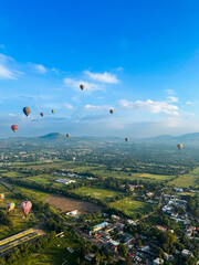Stunning aerial view of colorful hot air balloons flying over a Mexican town and green valley with mountains under a clear blue sky.