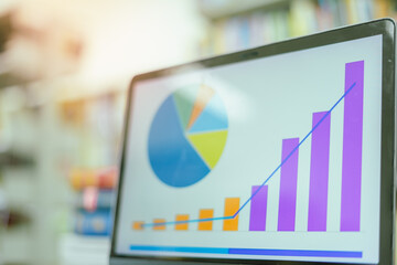 A laptop screen displaying a graph and a book placed on the table in the library, representing a business concept.	