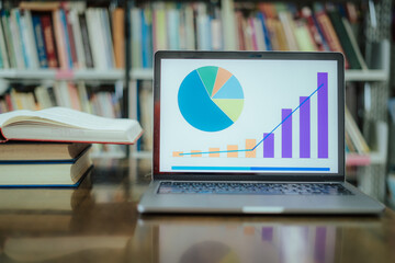A laptop screen displaying a graph and a book placed on the table in the library, representing a business concept.	