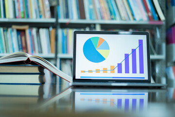 A laptop screen displaying a graph and a book placed on the table in the library, representing a business concept.	