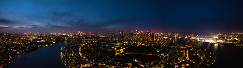 Naklejka premium Panorama of London skyline at night showcases vibrant city lights and the Thames River, aerial drone shot.