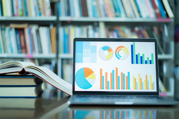 A laptop screen displaying a graph and a book placed on the table in the library, representing a business concept.	