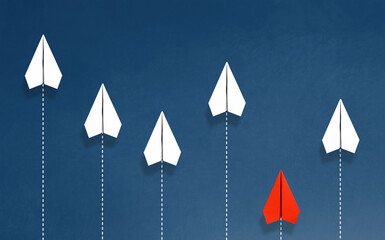 A red paper airplane flying downwards, distinct from five white paper airplanes flying upwards against a blue background, symbolizing individuality and going against the norm.