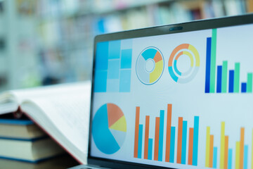 A laptop screen displaying a graph and a book placed on the table in the library, representing a business concept.	