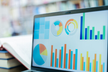 A laptop screen displaying a graph and a book placed on the table in the library, representing a business concept.	