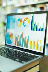 A laptop screen displaying a graph and a book placed on the table in the library, representing a business concept.	