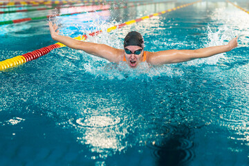 Woman swimmer in goggles and cap executes butterfly stroke in an indoor pool during a race.