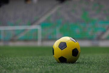 Fototapeta premium A yellow and black soccer ball rests on lush grass inside a large stadium, ready for an exciting match to begin.