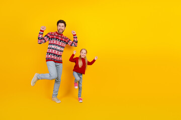 Father and child excitedly jumping against bright yellow background in festive sweaters, symbolizing joy and holiday spirit
