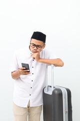 Confused asian muslim man carrying travel suitcase while using a cell phone. Going mudik or travel to hometown for Ramadan eid mubarak celebration