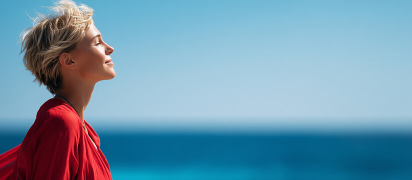 Joyful woman in red dress enjoying the breeze by the sea, smiling with her eyes closed, against a clear blue sky. - Powered by Adobe