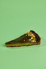 Enjoy a Delicious Slice of Chocolate and Pistachio Tart Beautifully Set on a Green Background