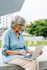 Senior woman using laptop outdoors in city park