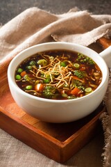 Indo-Chinese Manchow soup with fried noodles, vegetables, and spring onions in ceramic bowl