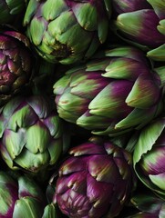 Fototapeta premium Fresh artichokes closeup. Macro flat lay of green and purple Italian artichokes with layered textured leaves.