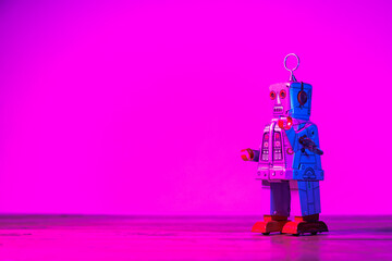 Retro tin wind-up robot toy standing on a wooden surface with a vibrant purple and red neon light background, creating a futuristic and nostalgic atmosphere