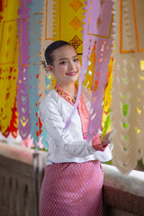 Woman in traditional attire smiles while standing beside colorful paper decorations, creating festive atmosphere