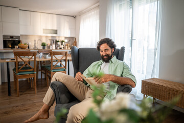 Man relaxing at home reading book in armchair