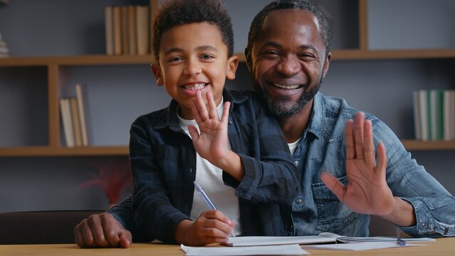 African American family smiling greeting hello portrait study looking at camera ethnic father dad with little son kid child boy studying learning at table writing homework distant education video call - Powered by Adobe