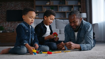 African American happy family playing with toys on floor at home carefree caring father with two...