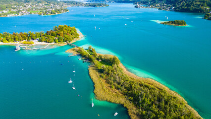 Aerial view of Portschach am Worthersee, Austria, with turquoise lake waters, boats, piers and alpine scenery. Popular summer holiday destination for relaxation, wellness and tourism