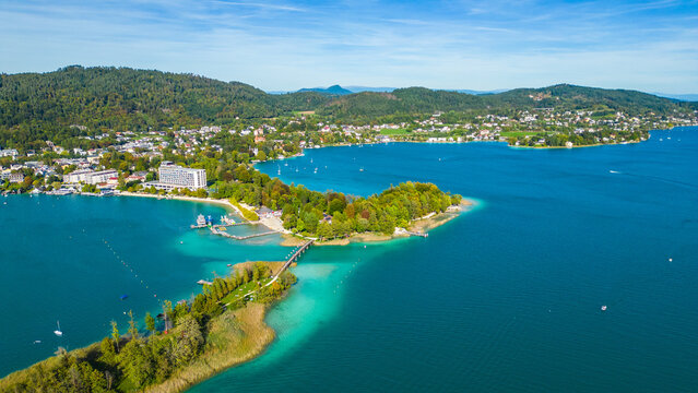 Aerial view of Portschach am Worthersee, Austria, with turquoise lake waters, boats, piers and alpine scenery. Popular summer holiday destination for relaxation, wellness and tourism