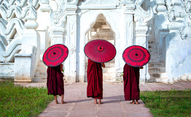 Three Asian young monk holding red umbrellas on the Mya Thein Tan Pagoda at Mingun, Mandalay Myanmar.