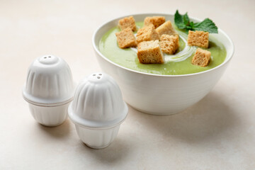 Salt and pepper shakers near bowl of delicious cream soup with croutons on light table, closeup