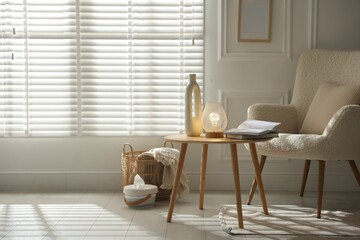Stylish lamp, vase and books on wooden table near armchair indoors, space for text