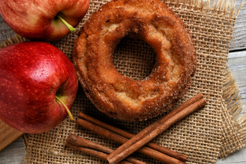 Apple Cider Donuts. Fresh made doughnuts on burlap napkins and a rustic white kitchen table with Gala Apples and Cinnamon Sticks.