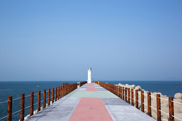Obraz premium White Lighthouse Standing Solitary on Rocky Coastline under Clear Sky