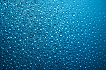 Top view of macro close up of bright blue water droplets densely covering a textured background under even lighting. Nature concept.