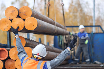 Construction workers manage heavy steel pipes at a site. The scene shows teamwork and safety in an...