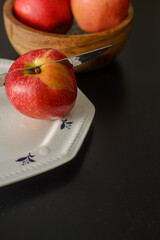 A knife that cut a red apple on a white plate