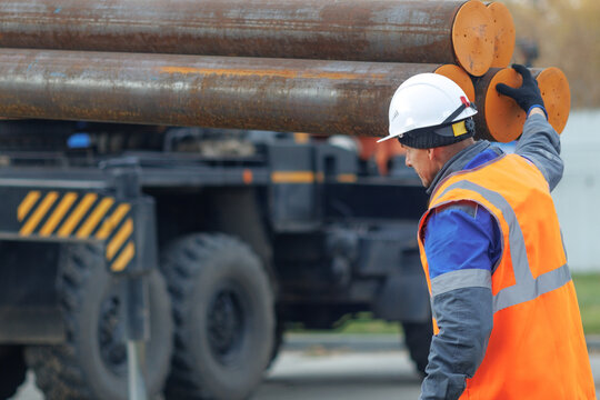 A construction worker in safety gear manages heavy steel pipes at a construction site, showcasing industrial work and safety practices.