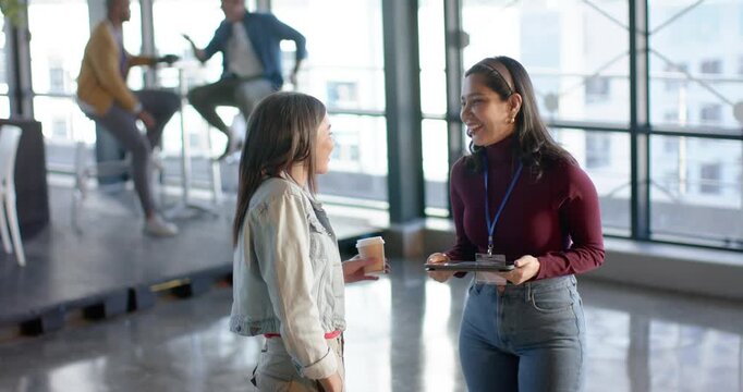 Diverse female colleagues exchanging greeting, checking clipboard, explaining plan in coworking hub