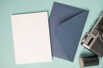 Empty white blank greeting or invitation card, envelope, vintage camera and film box on blue background.