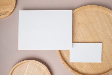 Empty white blank greeting or invitation card, name card, wooden plate on beige background. Mock up presentation.