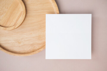 Empty white blank greeting or invitation card, wooden plate on beige background.
