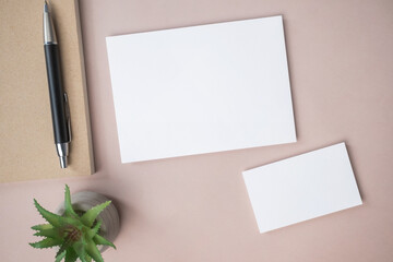 Empty white blank greeting or invitation card, name card, pen, note book, cactus on beige background.